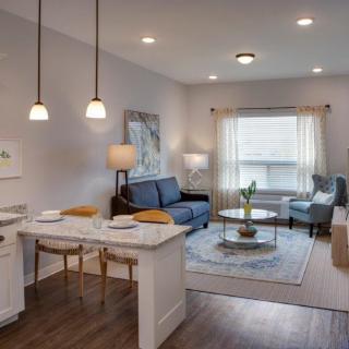 A cozy and modern living room featuring an open floor plan with a kitchen island, pendant lighting, and comfortable seating.