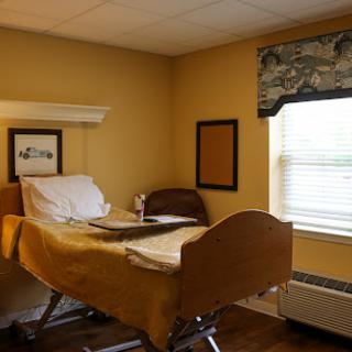 A comfortable hospital room featuring a bed, window with curtains, and warm yellow walls.