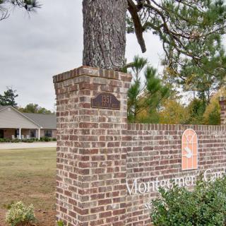 A brick pillar with a tree growing on top, displaying a sign near a residential building.