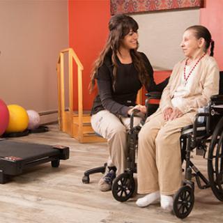 A caregiver interacts with an elderly woman in a rehabilitation setting, emphasizing support and care.