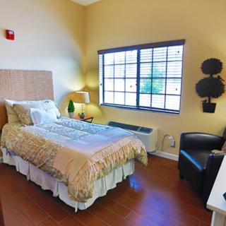 A cozy bedroom with a single bed, decorated in warm tones, featuring a window, chair, and table lamp.