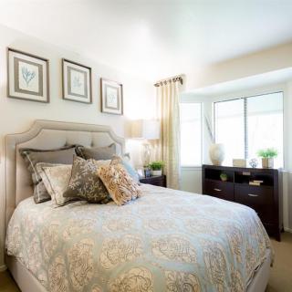A well-decorated bedroom featuring a cozy bed with patterned bedding, a dresser near a window, and elegant drapes.