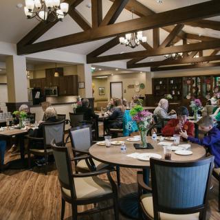 A communal dining area with wooden beams and chandeliers, where people are seated at tables.