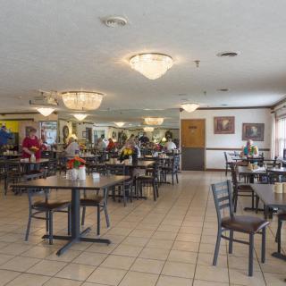 A spacious cafeteria with tables and chairs, featuring chandeliers and people dining.