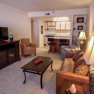 A cozy living room with a sofa, armchairs, and a view of the kitchen area.