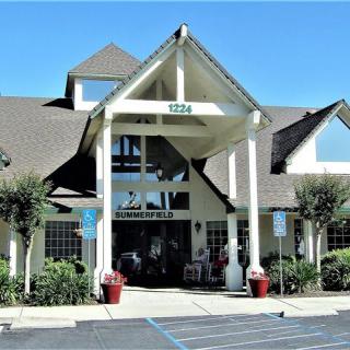 A front view of a building with a peaked roof and large entrance, surrounded by a parking lot.