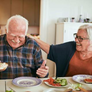 An elderly couple sharing a joyful moment while having a meal together at home.