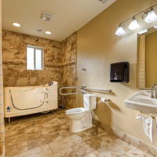 An accessible bathroom featuring a walk-in tub, toilet, sink, and grab bars with tile flooring.