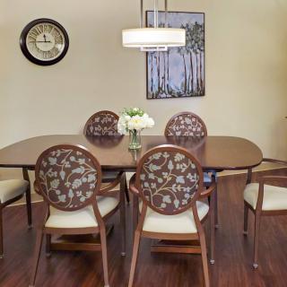 A cozy dining room with a wooden table and floral pattern chairs, illuminated by a pendant light, featuring wall art and a clock.
