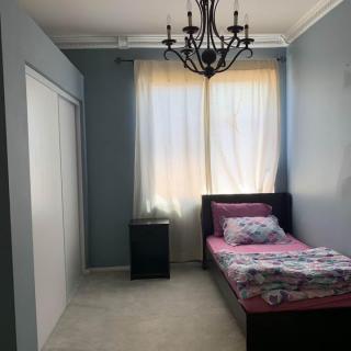 A minimalist bedroom with a single bed, chandelier, and soft curtains.
