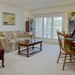 A cozy living room with a sofa, coffee table, dining area, and large windows.