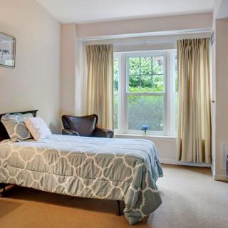 A cozy bedroom featuring a single bed with patterned bedding, a large window with curtains, and natural daylight.