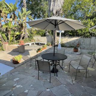 A sunny patio with outdoor seating and a large umbrella, surrounded by lush greenery.