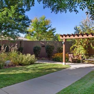 A serene garden featuring a pathway leading to a shaded pergola surrounded by lush greenery.