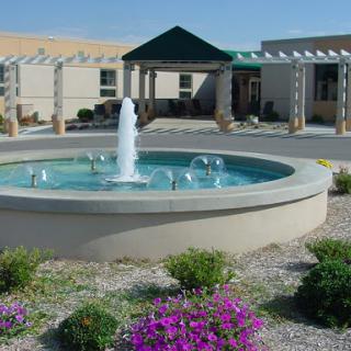 A serene outdoor setting featuring a fountain surrounded by colorful flowers and modern architecture.
