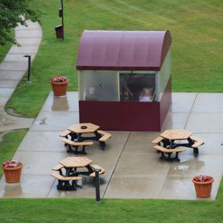 A cozy outdoor picnic area featuring a covered pavilion and several wooden tables set on a grassy lawn.