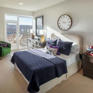 A modern bedroom with a bed, large wall clock, and a view of the balcony.