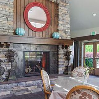 A cozy living room featuring a stone fireplace, adorned with a round mirror and decorative vases, complemented by a nearby table and chairs.