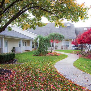 A serene garden pathway lined with colorful autumn leaves and surrounded by buildings.