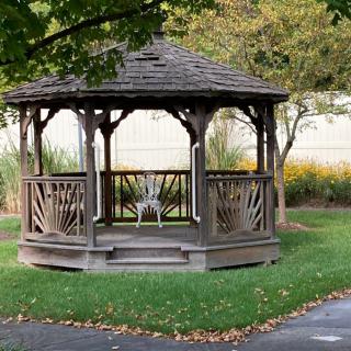 A wooden gazebo in a tranquil park setting, surrounded by trees and greenery.