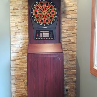 An electronic dart machine set against a stylish stone wall.