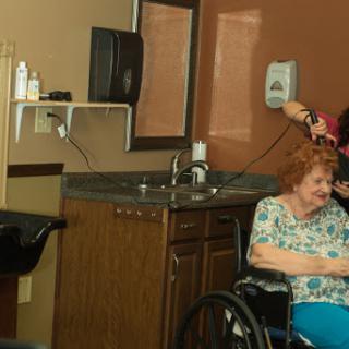 A caregiver assists an elderly woman in a salon setting, promoting personal care and companionship.