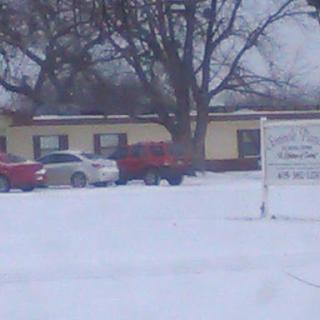 A snowy scene featuring parked cars in front of a building.