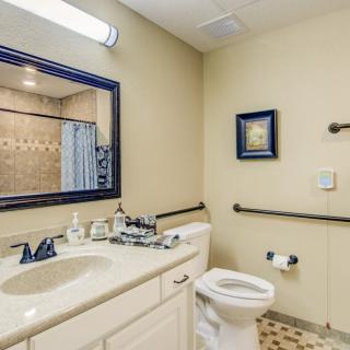 A well-lit bathroom featuring a sink, mirror, toilet, and shower with a decorative curtain.