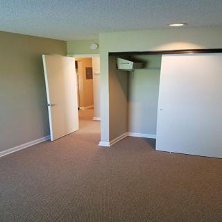An empty room with carpet flooring, featuring a closet and an open doorway.