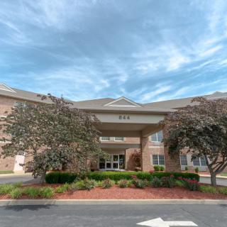 The front entrance of a brick building surrounded by trees and landscaping under a cloudy sky.