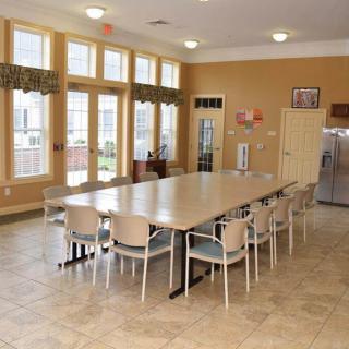 A spacious dining room with large tables and chairs, featuring big windows and a kitchen area.