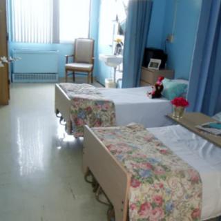 A hospital room with two neatly made beds and blue walls.
