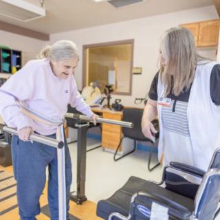 An elderly woman receiving assistance during a physical therapy session in a healthcare facility.