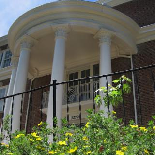 A close-up view of a classical-style building with prominent columns and blooming flowers in the foreground.