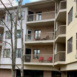 A view of an apartment building with multiple balconies, each adorned with outdoor furniture and surrounded by trees.