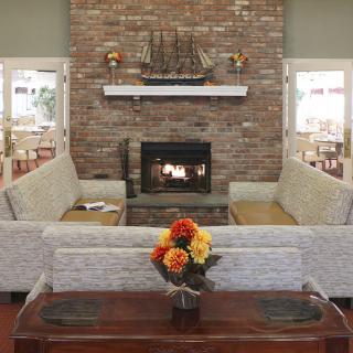 A cozy living room with a brick fireplace, surrounded by comfortable couches and a coffee table adorned with colorful flowers.