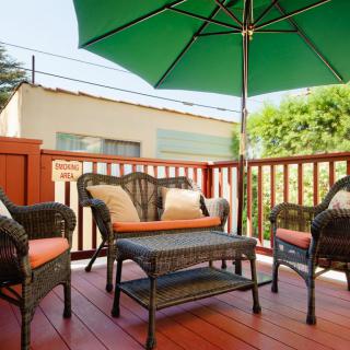 A cozy outdoor patio with wicker furniture and a green umbrella on a sunny day.