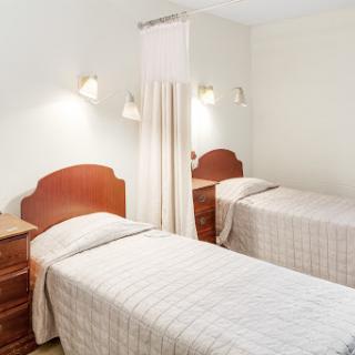 A cozy bedroom featuring two twin beds with simple decor and soft lighting.