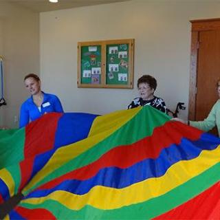 A group of people holding a colorful parachute indoors.