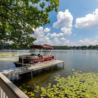 A serene lake scene with a docked boat and water lilies under a clear, blue sky.