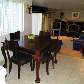 A dining area with a wooden table and chairs, adjacent to a living room featuring a television and fireplace.