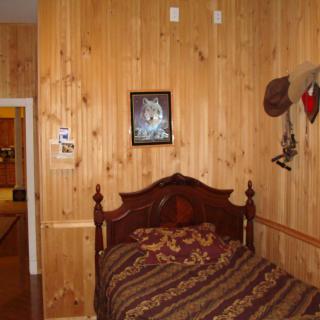 A cozy bedroom with wood paneling and rustic decor, featuring a single bed.