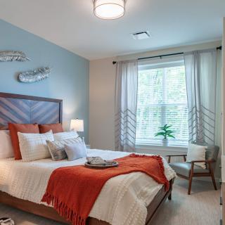 A modern and cozy bedroom with orange accents and ample natural light.