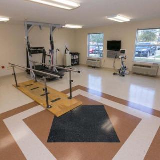 A physical therapy room equipped with rehabilitation equipment including a treadmill and parallel bars.