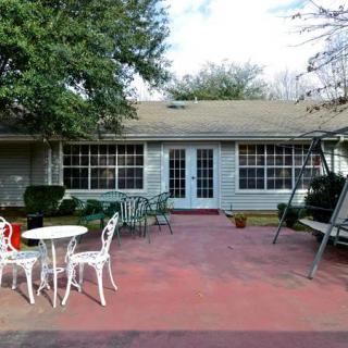 A cozy patio area with outdoor furniture, including a table, chairs, and a swing seat, in front of a house with large windows.