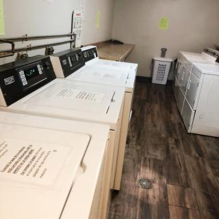 A laundry room with several washing machines and dryers on a wooden floor.
