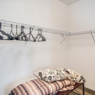 An empty walk-in closet with a row of hangers and neatly folded blankets on a shelf.