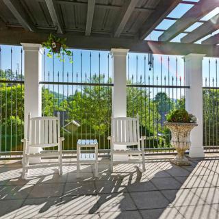 A sunny patio with white rocking chairs under a pergola, offering a serene garden view.