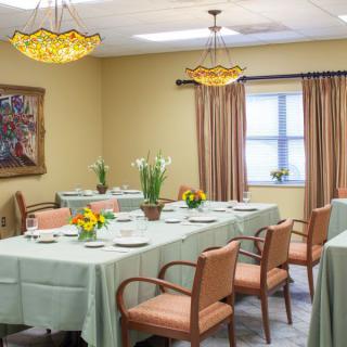 A neatly arranged dining room with tables set for a meal, decorated with flowers and elegant lighting.