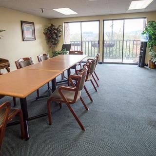 A spacious conference room with a long meeting table, surrounded by chairs and featuring large windows and indoor plants for a comfortable office environment.